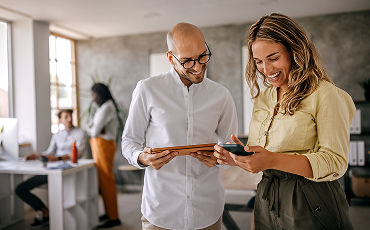  Man holding tablet and woman holding phone, smiling, looking down at their devices