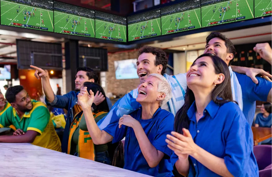 Customers celebrating and cheering with TV screens lining the walls of a restaurant or bar