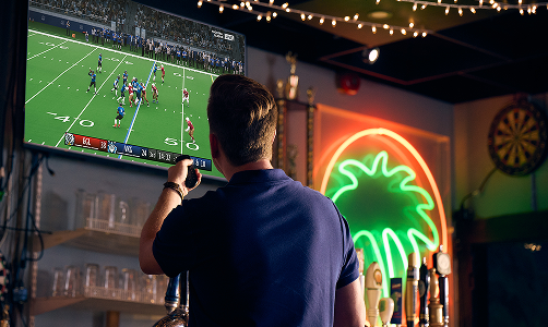 Man holding remote turning on a sports game at the bar