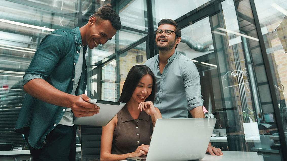 Happy to work together. Group of three young and positive employees using modern technologies and smiling while working in modern office